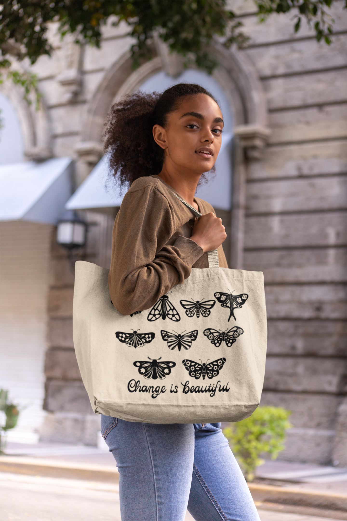 Woman holding a landscape canvas tote bag with black screen-printed artwork of moths and butterflies